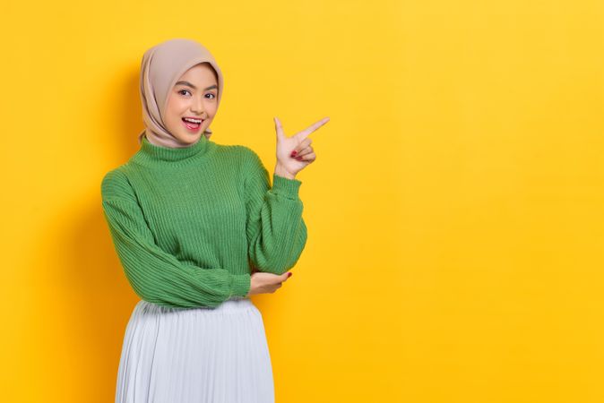 Excited woman in headscarf pointing her finger towards the side
