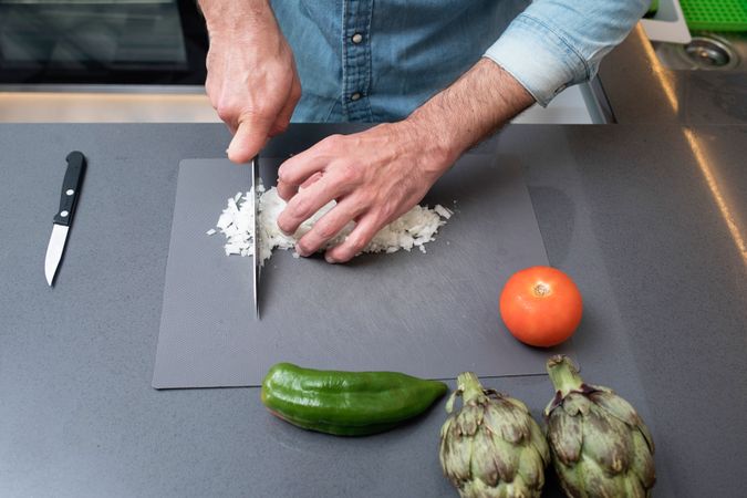 Hands of man prepping onion on board with knife