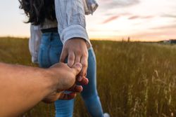 couple holding hands in a field with a beautiful sunset