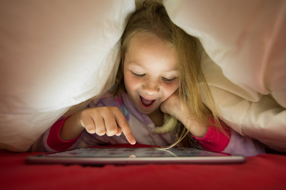Girl using tablet under blanket