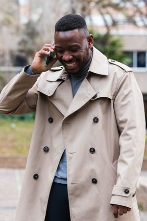 Happy Black man talking with smartphone standing on street