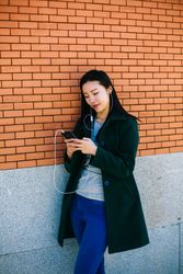 Asian female listening to music near brick wall