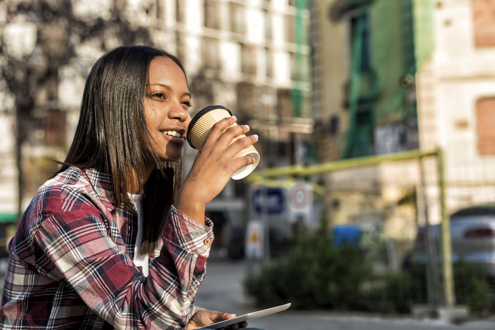 Female in plaid shirt sitting outside with tablet and to go drink