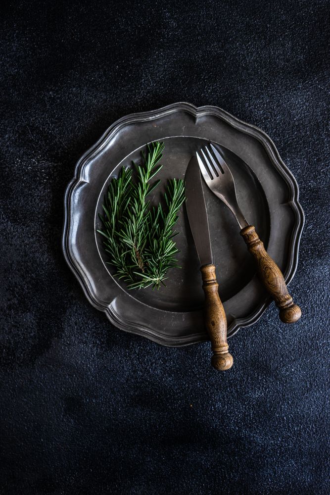 Table setting with dark plate with rosemary sprig