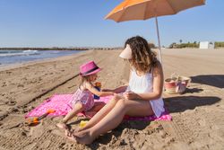 a girl putting sunscreen cream on her mother at the beach