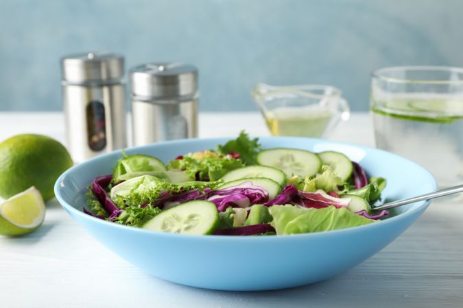 Plate with fresh salad, spices and oil on wooden background, close up