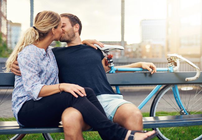 Cute couple kissing on bench taking a break while out on a bike ride