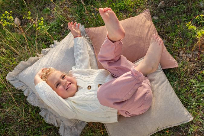 Cute girl lying on cozy pillow on glade in countryside
