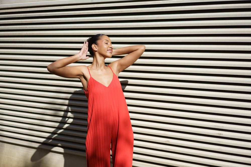 A Stylish Woman Wearing a Stunning Red Dress Posing Elegantly Against a Textured Wall