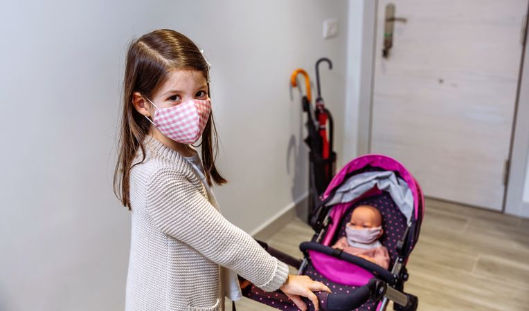 Girl with face mask ready to go for a walk with her doll with mask