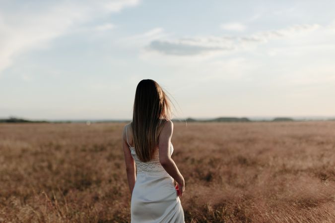 Back view of young woman in a dress standing in an open field