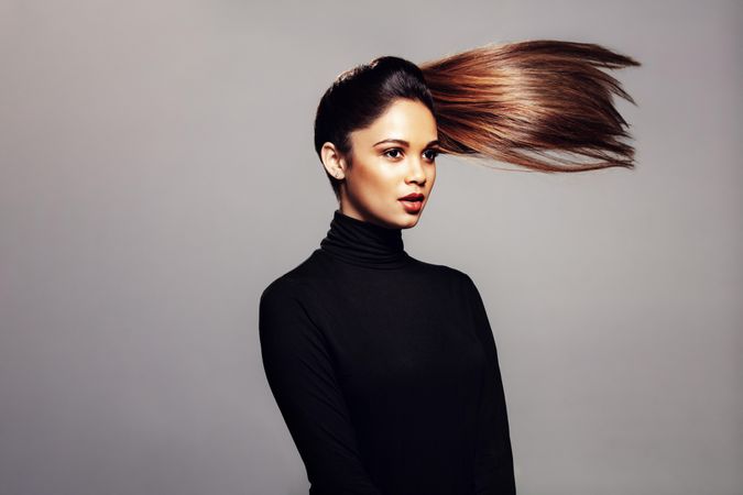 Studio shot of beautiful female against over grey background with hair ponytail flying in air