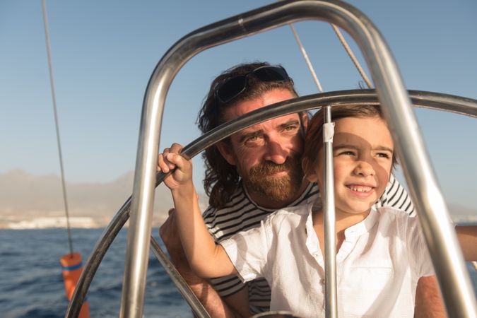 Man with boy holding steering wheel on yacht on water