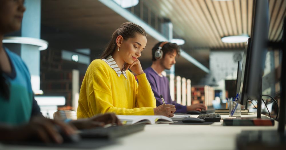 Group of Diverse High School Students Individually Studying in a Public Library. Young People Working Behind Computers, Read Textbooks, Take Notes in Notebooks, Write Essays and Prepare for Lectures