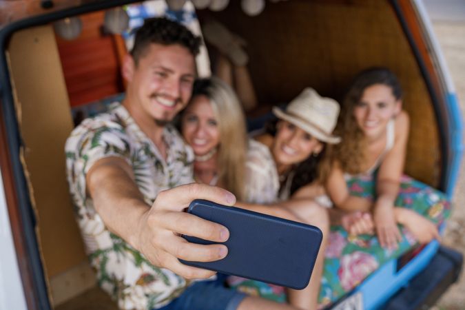 Smiling man taking selfie with girlfriends comfortable placing on trunk of blue car