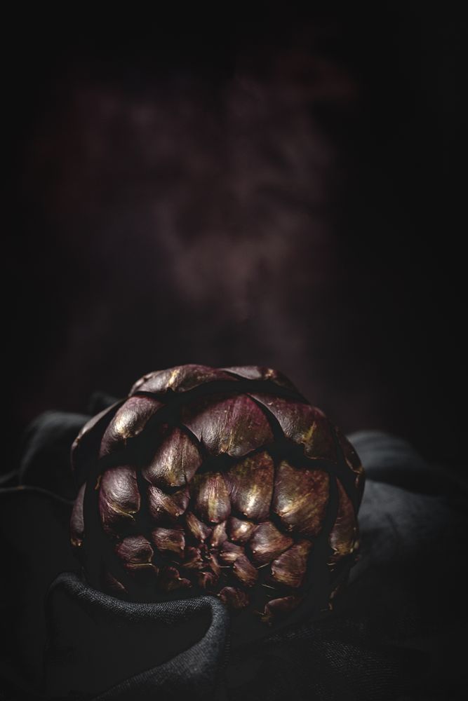 Fresh raw purple artichokes on dark background.