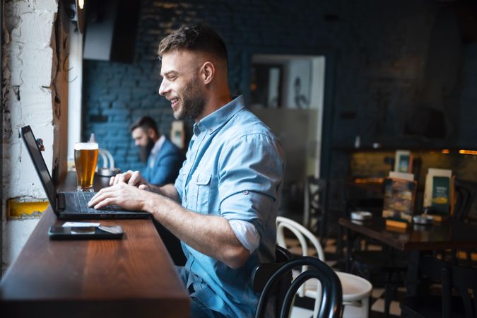 Man smiling at laptop with beer in pub at lunch time
