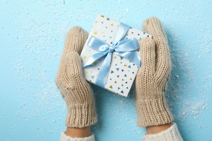 Girl holding in hands present on blue background with snow, space for text
