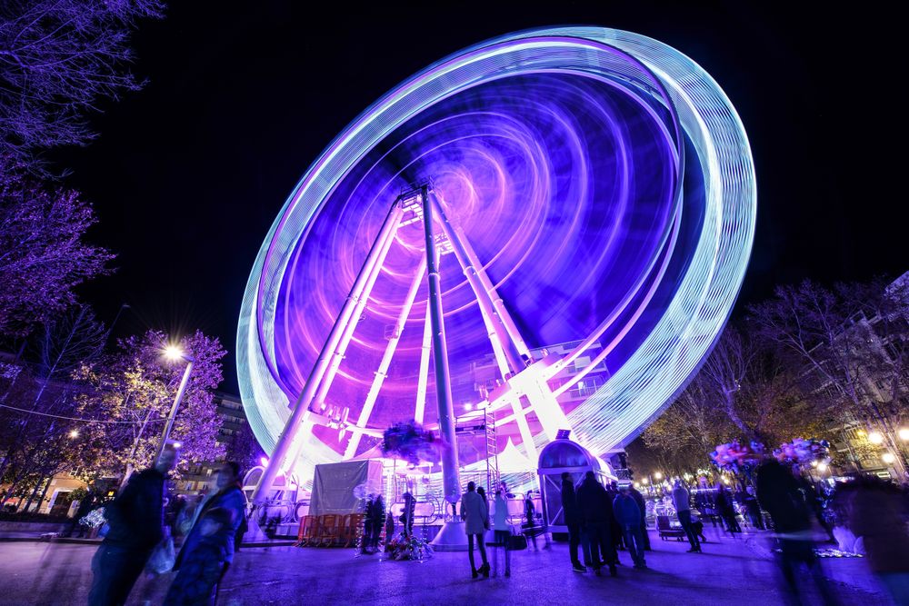 Purple lit ferris wheel with people walking around park