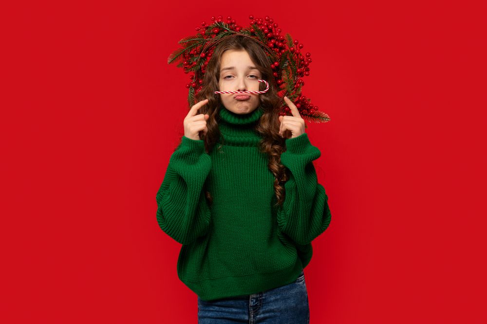 Young girl in green sweater balancing candy cane mustache