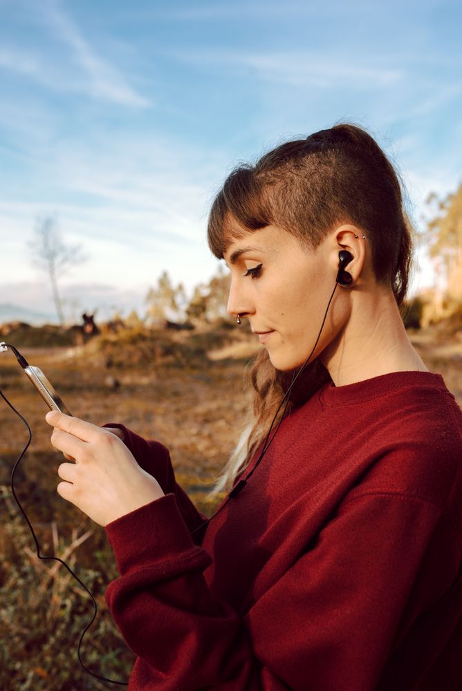 Young woman with piercing listening music on smartphone on hill