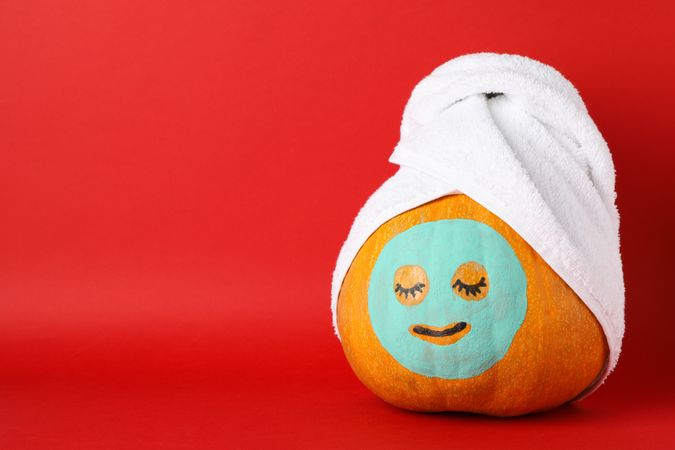 Pumpkin with facial mask and towel on red background, copy space