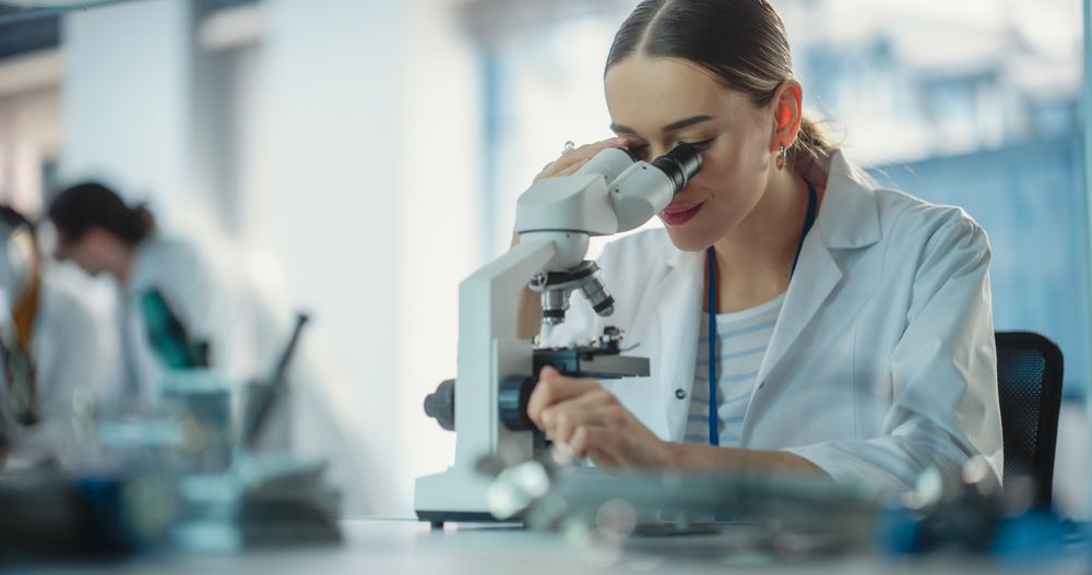 Portrait of Young Professional Female Engineer Using a Microscope in a Lab to Examine an Electrical Component.