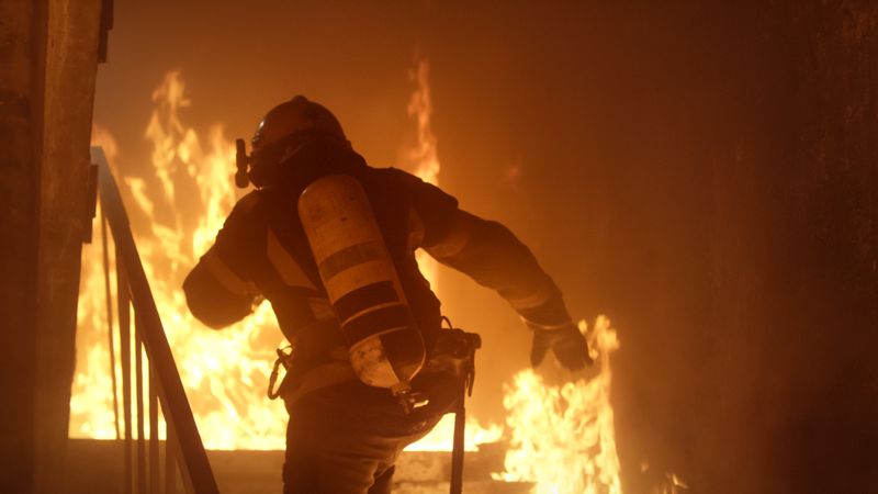 Firefighter running up stairs toward raging fire