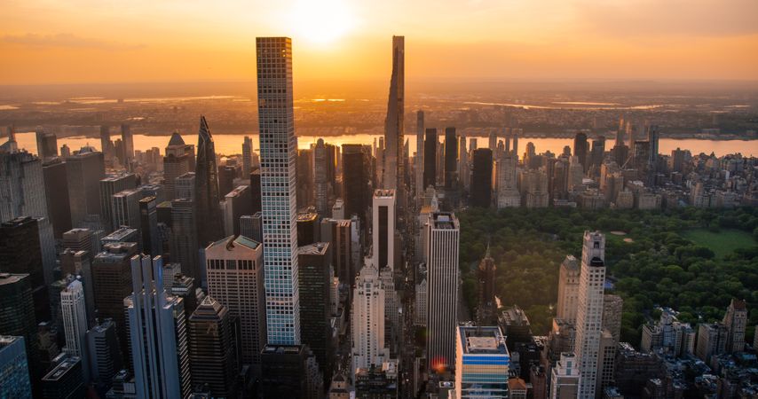 New York Cityscape at Sunset. Aerial Shot from a Helicopter. Modern Skyscraper Buildings with Central Park in Manhattan Island. Focus on City Architecture Next to Park