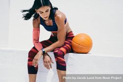 Slender woman sitting with basketball on wall ledge 4ZOlxb