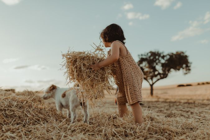 Little girl lifting a pile of hay with a dog in the background