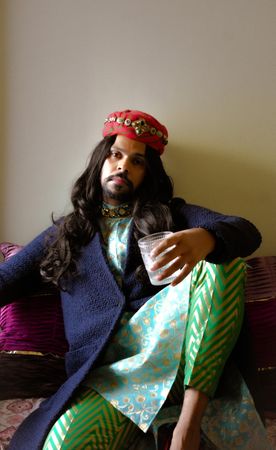 Indian man with long hair sitting on floor holding a drink