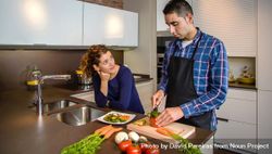 Woman talking to man as he cuts vegetables for dinner bx2ar5