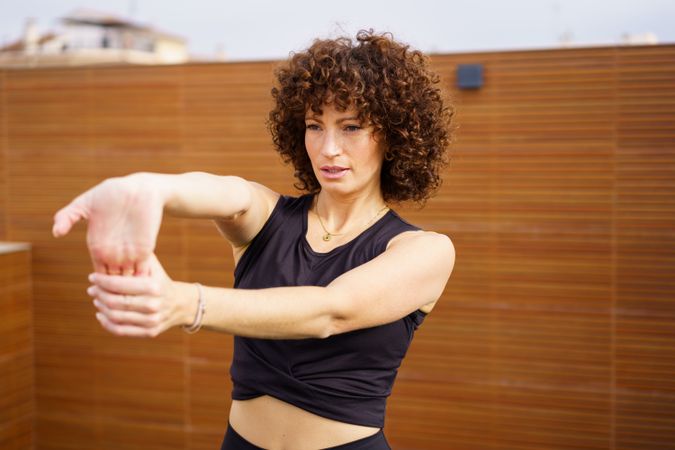 A Woman Enthusiastically Stretching on a Rooftop with Beautiful Curly Hair in the Sunshine