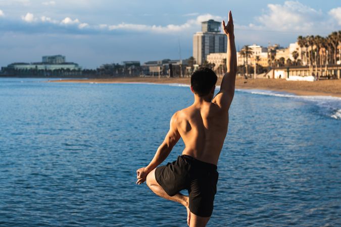 Shirtless man balancing in yoga pose on beach