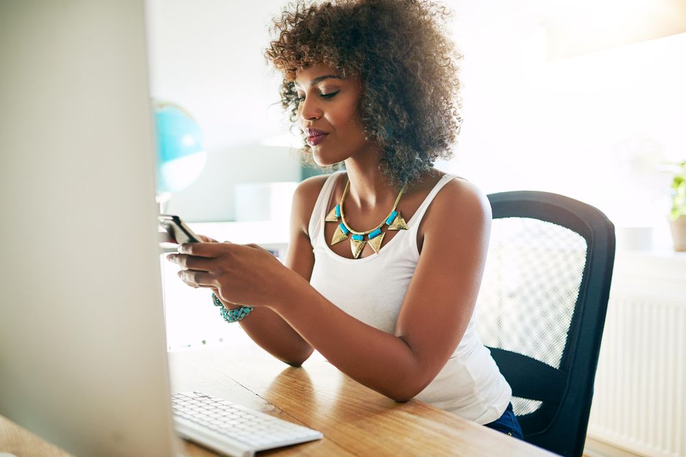 Content curly haired female at her home office desk checking her phone messages