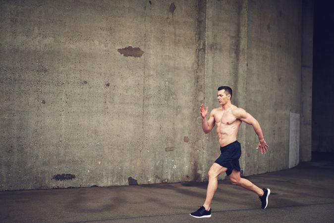Shirtless muscular man running against a concrete wall