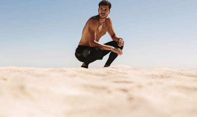 Fit male crouching and looking to the side during workout on seashore