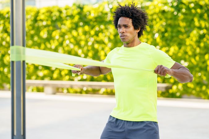 Man pulling back on resistance bands with arms in front of hedge