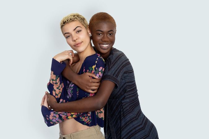 Photo of two multiethnic joyful woman embrace while looking at camera