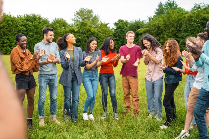 Multiethnic group of young people in circle applauding outdoors