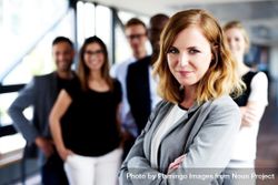 Business woman smiling with her arms crossed in front of colleagues at work 0PwVgb
