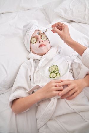 Unrecognizable mother applying mask on face of child during spa