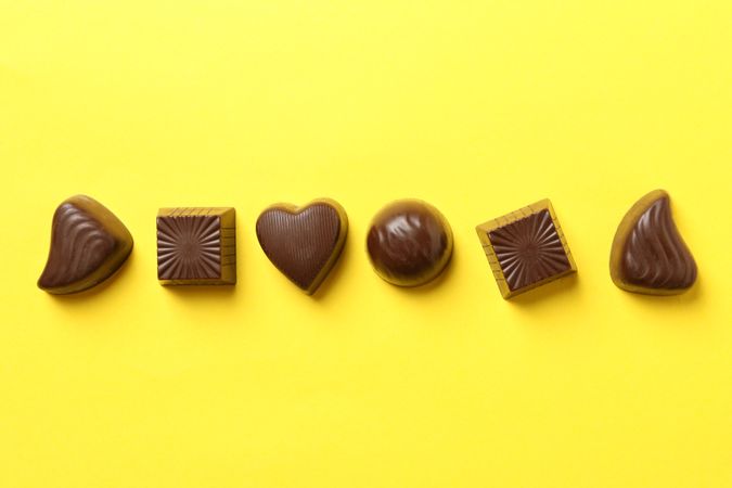 Tasty chocolate candies on yellow background, top view