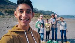 Young man taking selfie to group of volunteers after cleaning beach
