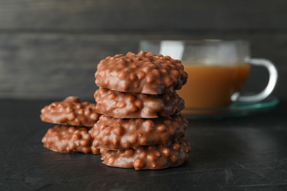 Stack of chocolate cookies and cup of coffee on table against wooden background