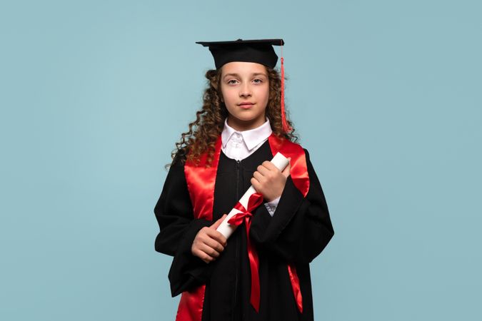 Young girl in graduation attire holding diploma with serious expression
