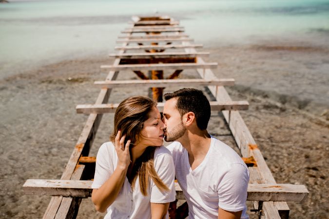 Glad lovers sitting on destroyed pier on seashore