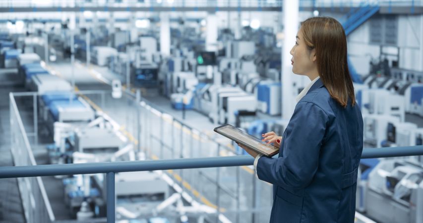 Portrait of a Japanese Engineer Using Tablet Computer and Looking Around a Factory Facility with Equipment Producing Modern Electronic Components for Different Industries