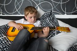 Young blonde boy playing toy guitar